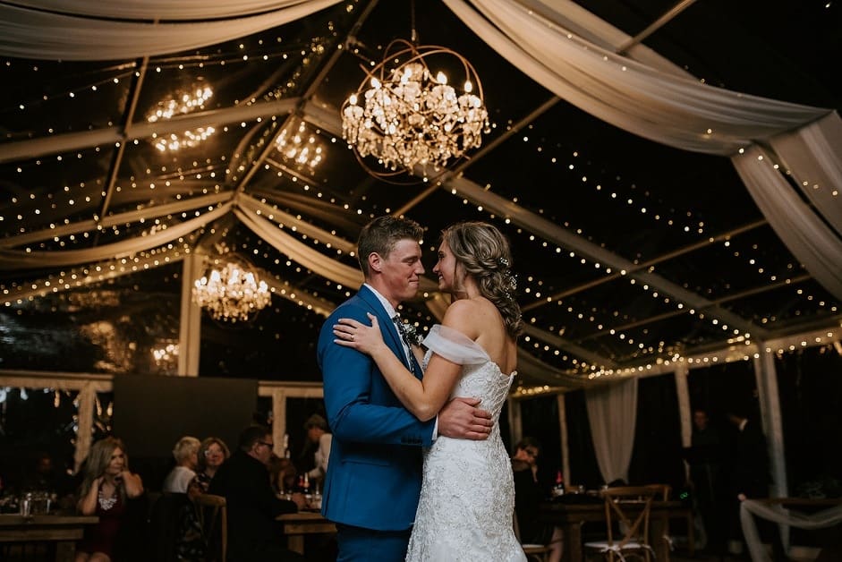 bride and groom dancing in a clear tent with ceiling draping and chandeliers in ponoka